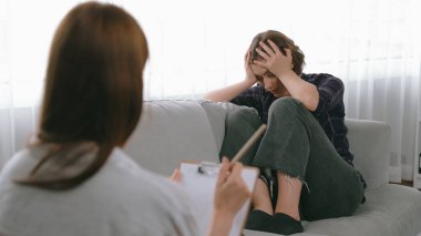 Psikologla ruh sağlığı terapisi gören üzgün travma sonrası stres bozukluğu olan bir kadın. Yaşam sonrası depresyon veya keder. Hayal kırıklığına uğramış genç bir kadın klinikteki duygular hakkında prim psikoloğuyla konuşuyor.