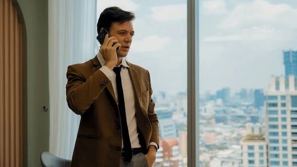 Businessman standing in ornamented office talking on phone with college on cityscape skyline window background. Determination and ambition drive business career toward to bright future