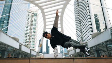 Genç Asyalı hippi şehir merkezinde insanların etrafında ayak izlerini gösteriyor. Şık bir sokak dansçısı B-boy ya da serbest dans eder. Açık hava sporu 2024. Break dans. Yumuşak bir şekilde..