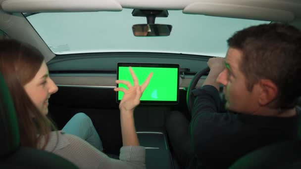 度假公路旅行与环保汽车的概念 环保意识很强的年轻夫妇坐在驾驶座上 手持空白复制空间的绿色荧幕车显示器 以检测电动车的电池状态 高级备选案文 — 图库视频影像