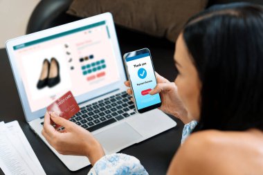 Genç bir kadın dizüstü bilgisayarla ürün sipariş eder ya da satın alır ve akıllı telefondan işlem ödemesi yapar. İnternet bankacılığı vasıtasıyla internet üzerinden kredi kartıyla online alışveriş hayatı. Blithe