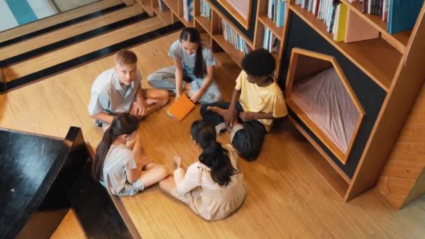 不同的孩子围坐在一起 看着相机 挥手看着图书馆 周围堆满了书 多元文化高中学生问候相机 — 图库视频影像