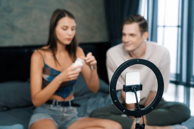 Sosyal medya için güzellik ve kozmetik video içeriği hazırlayan genç bir kadın erkek arkadaşını model ve ışık yüzüğü olarak kullanıyor. Güzellik blogcusu seyirciye ya da takipçiye güzellik bakımını gösteriyor. Açılıyor