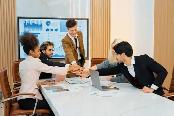 Corporate diverse businesspeople putting hands together on meeting table with document scatter around at business meeting room. Represented unity, cooperation, collaboration, corporate. Ornamented.