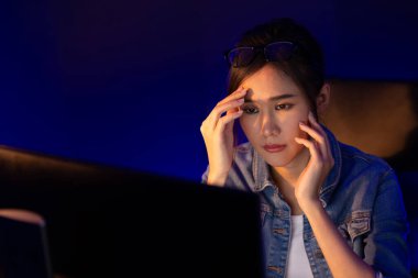 Stresli, genç, güzel Asyalı yaratıcı proje yaratıcısı sosyal medyayı araştırmak için bilgisayara bakıyor ve geceleri daha çok neon modern ofisin planlama kanalı stratejisine ulaşılıyor. Taktik.