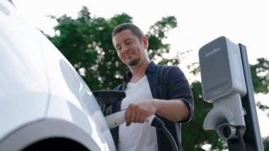 Yolculuk sırasında doğal orman ya da milli parktaki elektrikli araba için şarj olan bir adam. Tatil ve tatil boyunca çevre dostu seyahat. Yükselt