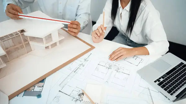 Professional engineer measures house model while skilled designer writes down in blueprint. Work together, collaboration, cooperate. Creative design and team working concept. Closeup. Immaculate