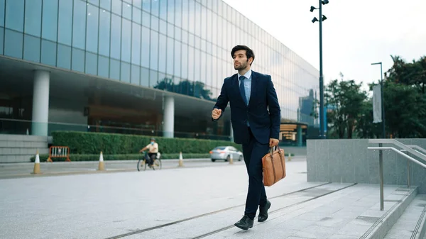 Smart business man walking to office while calling his business team about startup project. Handsome male leader report about marketing plan by using phone while going to meeting room. Exultant.