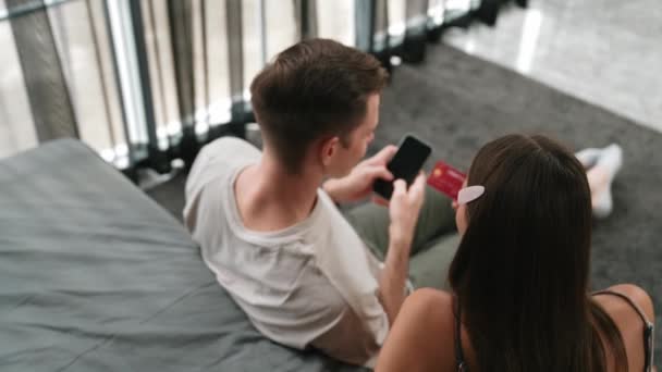 Νεαρό Ζευγάρι Κάθεται Στο Υπνοδωμάτιο Σπίτι Χρησιμοποιώντας Online Εφαρμογή Πληρωμής — Αρχείο Βίντεο