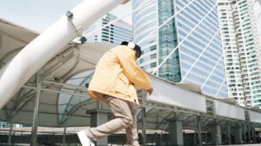 Asyalı şık bir adam alçak açılı kamerayla hip hop dansı yapıyor. Break dansçı, şehirde kulaklıktan müzik dinleyip dans ederken merdivenlerden çıkıyor. Açık hava sporu 2024. Yumuşak bir şekilde..