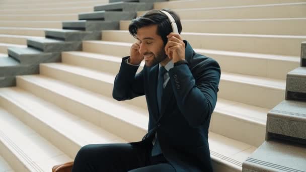 由专业商人组成的团体喜欢用耳机听音乐 聪明的项目经理坐在楼梯上时戴耳机的肖像 接受好消息 得到晋升 膨胀剂 — 图库视频影像