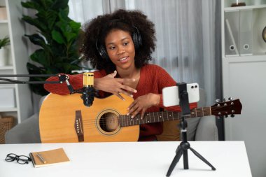 Genç Afrikalı Amerikalı müzisyenin sunucu kanalı gitar çalıyor, şarkı söylüyor, stüdyoda akıllı telefondan yayın yapıyor. Ekipman kulaklıkları dekorasyonu ve mikrofon kaydı. Tatlandırıcı.