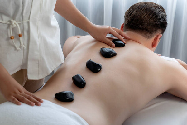 Массаж горячими камнями в спа-салоне на роскошном курорте с дневной легкой атмосферой спокойствия, блаженный клиент, наслаждающийся спа-массажем из базальтового камня скользит по телу с успокаивающим теплом. Quiescent