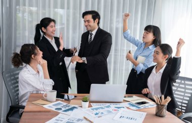 Kutlama jesti ve başarılı takım çalışması yapan bir grup mutlu iş adamı. Çeşitli yarış bürosu çalışanları şirket ofisinde pazarlama planlamasında ilerleme kaydettikten sonra kutlama yapıyorlar. Habiliment