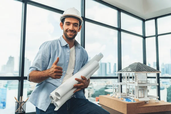 Portrait of professional architect engineer thinking about modern house project while wearing safety helmet and casual outfit. Smart interior designer holding project plans near house model. Tracery.