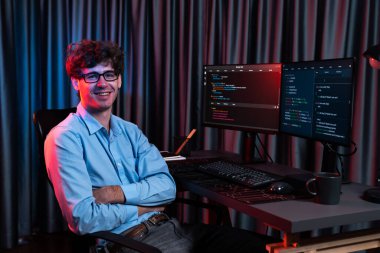 Ekranda yazılım geliştirme bilgisine karşı oturan gülümseyen bilişim geliştiricisinin profili, web sitesindeki son sürüm uygulaması için program kodlaması oluşturarak çevrili kameraya bakıyor. Toplayıcı.