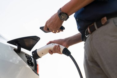 Genç adam, alışveriş merkezinin otoparkındaki EV otomobil şarj istasyonunda elektriği ödemek için akıllı telefonu kullanıyor. Modern çevre ve EV araçlı sürdürülebilir şehir yaşam tarzı. Yararlı