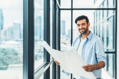Proje planı yaparken gökdelen ve şehir manzarasına bakan günlük kıyafetli profesyonel mimar ya da erkek işçi. Yaratıcı tasarım, inşaat mühendisliği, bina inşaatı. İzleme.