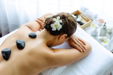 Lüks tatil köyündeki kaplıcalarda sıcak taş masajı. Gün ışığı sükunet ortamında, mutlu kadın müşteri bazalt taş masajından zevk alıyor. Rahatlatıcı bir sıcaklıkla vücudun üzerinde süzülüyor. Sessiz.