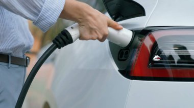 Yolculuk sırasında doğal orman ya da milli parktaki elektrikli araba için şarj olan genç bir kadın. Tatil ve tatil boyunca çevre dostu seyahat. Yükselt