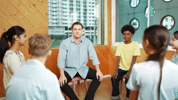 Smart teacher talking about mental health problem and sharing idea with boy during group therapy. Happy instructor pointing at children while explain plan while student listening idea. Edification.