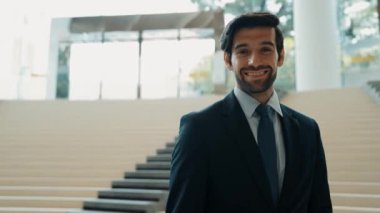 Akıllı iş adamı merdivenlerde kameraya bakıyor. İş elbisesi giyerken kameraya gülümseyen başarılı adamın yakın çekimi. Yönetici, kameraya bak. Hareket eden kamera. Sevinçli..