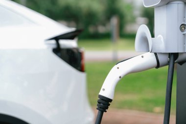 Açık yeşil şehir parkı manzarasındaki EV şarj istasyonundan EV elektrikli araç şarj oluyor. Çevre dostu EV araba yolculuğuyla doğal koruma. Yükselt