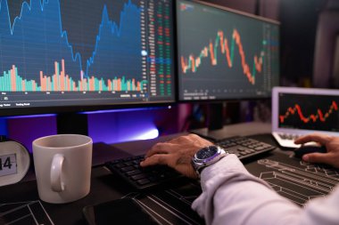 Akıllı tüccar işadamlarının elleri dinamik borsa yatırımlarına yoğunlaşarak bilgisayar ve dizüstü bilgisayara odaklanarak karanlıkta neon ışıklı ofisteki arama pazarında yüksek kar elde ettiklerini gösteriyor. Tahmin et..