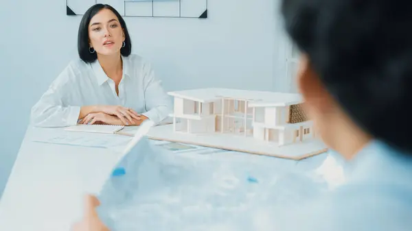 Professional asian male project manager hand puts the map on meeting table while discuss and brainstorm with coworker about building project at meeting room with blueprint hand behind. Immaculate.