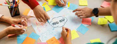 Profesyonel başlangıç grubu zihin haritası kullanarak yaratıcı pazarlama fikrini paylaşıyor. Genç yetenekli iş adamları yapışkan notlar yazarken beyin fırtınası planı yapıyorlar. Eline odaklan. - Yakın çekim. Değiştirilmiş.