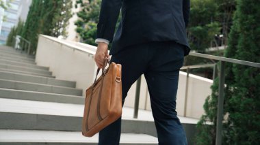 Yeşil şehirde bavulunu tutarken resmi takım elbiseli beyaz bir müdürün merdivenlerden çıkışının arka görüntüsü. Profesyonel bir iş adamı iş yerine giderken aynı zamanda Eko Şehri 'nde merdivenleri çıkıyor. Urbane..