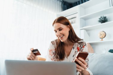 Genç mutlu kadın internetten alışveriş yaparak ürün satın alırken aynı zamanda internet üzerinden online ödeme sistemi ile çevrimiçi mağaza platformundan en yüksek siber güvenlik tarafından korunan ürünler sipariş ediyor.