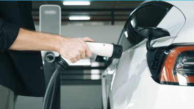 Genç adam EV elektrikli arabasıyla şehir merkezindeki alışveriş merkezinin otoparkına gidiyor şehir merkezindeki sürdürülebilirlik yaşam tarzını yeşil, temiz, yeniden şarj edilebilir elektrikli araç iç organlarıyla şarj ediyor.