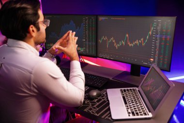 Akıllı tüccar işadamı, karanlık oda gecesinde neon ışıklı ofisteki arama pazarında yüksek kârla ekranda bilgisayar ve bilgisayar üzerinde dinamik borsa yatırımları üzerinde yoğunlaşıyor. Tahmin et..