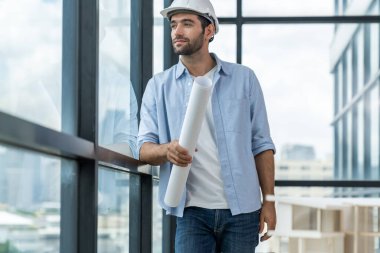 Akıllı inşaat mühendisi ev modeli ve mimari ekipmanlara bakarken ayakta duruyor, yürüyor. Kasklı bir mühendis bina modelinin yanında dururken şehir manzarası yakınında duruyor. İzleme.