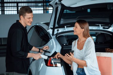 Genç çift EV elektrikli arabasıyla alışveriş merkezinin otoparkına gidiyor şehir merkezindeki şarj oluyor yeşil temiz şarj edilebilir elektrikli araç iç organları ile kentsel sürdürülebilirlik yaşam tarzını gösteriyor