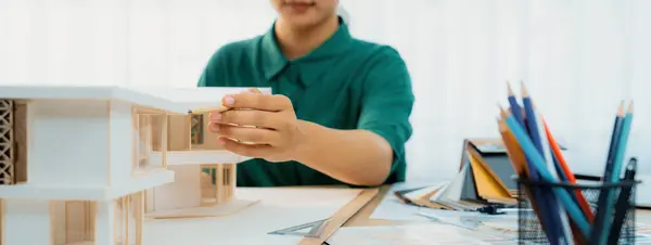 女性デザイナーをイメージしたクロップドは 家のモデルとテーブルの上に置かれたカラーウォッチとの彼女の仕事に意図的に焦点を当てて鉛筆で家モデルを測定します 手で集中する クローズアップ ヴァリーゲート — ストック写真