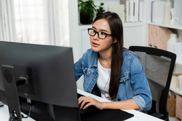 年轻美丽的亚洲创意经理 戴着眼镜打字 在社交媒体上设计了新的网站 在现代家庭办公室里穿着蓝色牛仔裤衬衫 在Pc上搜寻 Stratagem — 图库照片