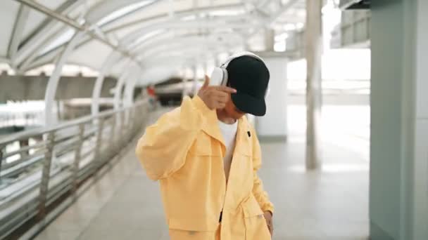 亚洲嬉皮士移动到嘻哈音乐和挥手的服装 专业的霹雳舞者一边走路 一边看着镜头 戴着耳机 穿着时髦的衣服 2024年户外运动 神气活现 — 图库视频影像