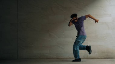 Zeki sokak dansçısı, gri arka planlı bir binada break dansçı hareketi yapıyor. Genç ve çekici koreograf enerjik ve aktif hareket ediyor. Açık hava sporu 2024. Yumuşak bir şekilde..