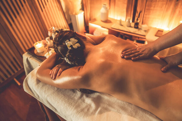 Closeup woman customer enjoying relaxing anti-stress spa massage and pampering with beauty skin recreation leisure in warm candle lighting ambient salon spa at luxury resort or hotel. Quiescent