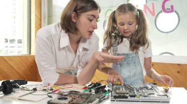 Genç, zeki, beyaz bir öğretmen öğrencilere elektronik kurulun bir parçasını öğretiyor. Uzman kız dijital elektrikli aletleri öğreniyor ve cips ve kablolarla ana kartı tamir ediyor. Etkinlik.