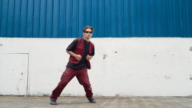 Beyaz arka planda break dans pratiği yapan yakışıklı bir sokak dansçısı. Hip hop tarzı giyinen sporcu, mavi arka planlı bir sokakta müzik eşliğinde ayak sesleri çıkarıyor. Açık hava sporu 2024. ÇalışmaComment.