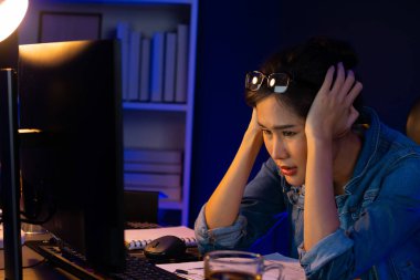 Stresli, genç, güzel Asyalı yaratıcı proje yaratıcısı sosyal medyayı araştırmak için bilgisayara bakıyor ve geceleri daha çok neon modern ofisin planlama kanalı stratejisine ulaşılıyor. Taktik.