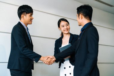 İş adamları konsepti kabul ediyor. İş adamı toplantı odasında başka bir iş adamıyla tokalaşıyor. Genç Asyalı sekreter bayan onların yanında duruyor. uds