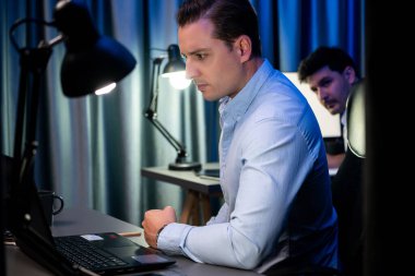 Stresli işadamı, iş ortağının iş yerinin ışıklı dizüstü bilgisayarında sorunu çözmek için iş ortağının desteğiyle son teslim tarihi için e-posta göndermeyi bekliyor. Satılabilir.