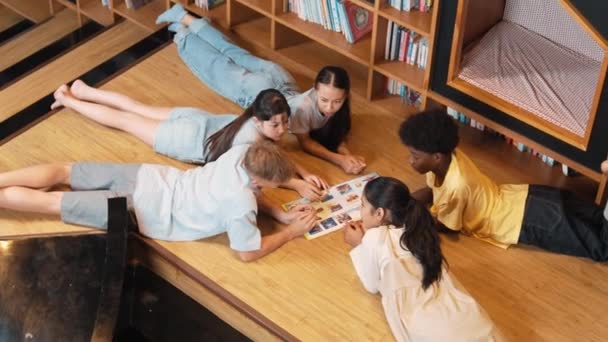 一群各种各样的孩子在图书馆看书时 成圈地躺着 女孩一边指点感兴趣的话题 一边和可爱的朋友聊天 一边分享杂志的头像 — 图库视频影像