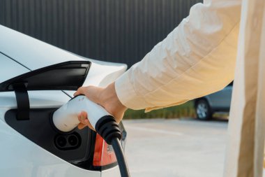 Genç bir kadın şarj aletini şarj istasyonundan elektrikli araba aküsünü şarj etmek için kullanmış. Sürdürülebilir çevre dostu seyahat konsepti için alternatif enerji ve şarj edilebilir EV araba. Yararlı