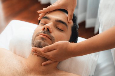 Beyaz adam stres önleyici kafa masajından ve lüks bir tatil beldesi veya otel spa salonundaki modern ışık ortamında yüz güzelliği eğlencelerini şımartmaktan hoşlanıyor. Sessiz.