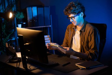 Genç iş adamı, yeni bir proje için deftere bakıyor. Neon Light Modern Ofis 'te masa başına. Pazar kanalı tasarım kavramında pazarlama ağında çevrimiçi planlama. Toplayıcı.